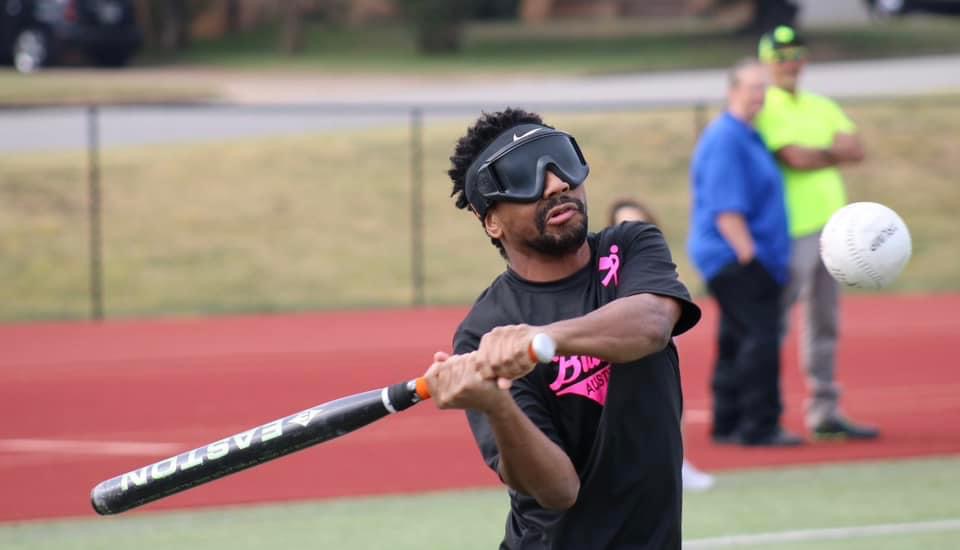 Darius, wearing a blindfold, leans to the side with a bat over his shoulder in position to swing at the ball.
