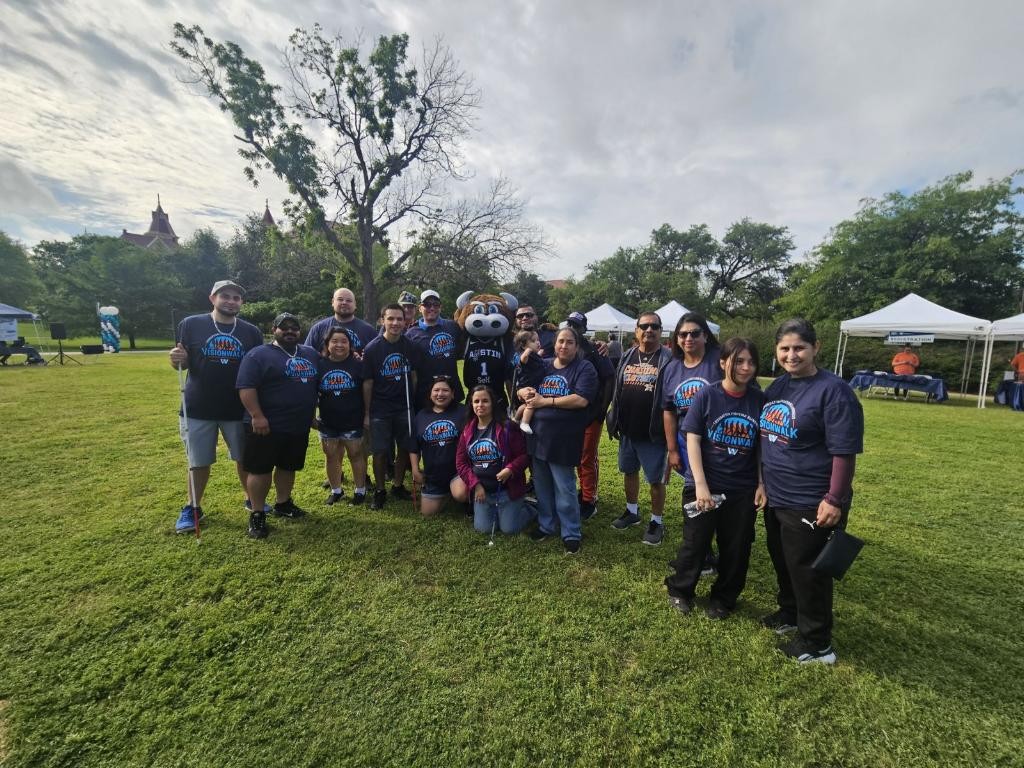A group of people in VisionWalk shirts pose with the Austin Spurs mascot, Da Bull.